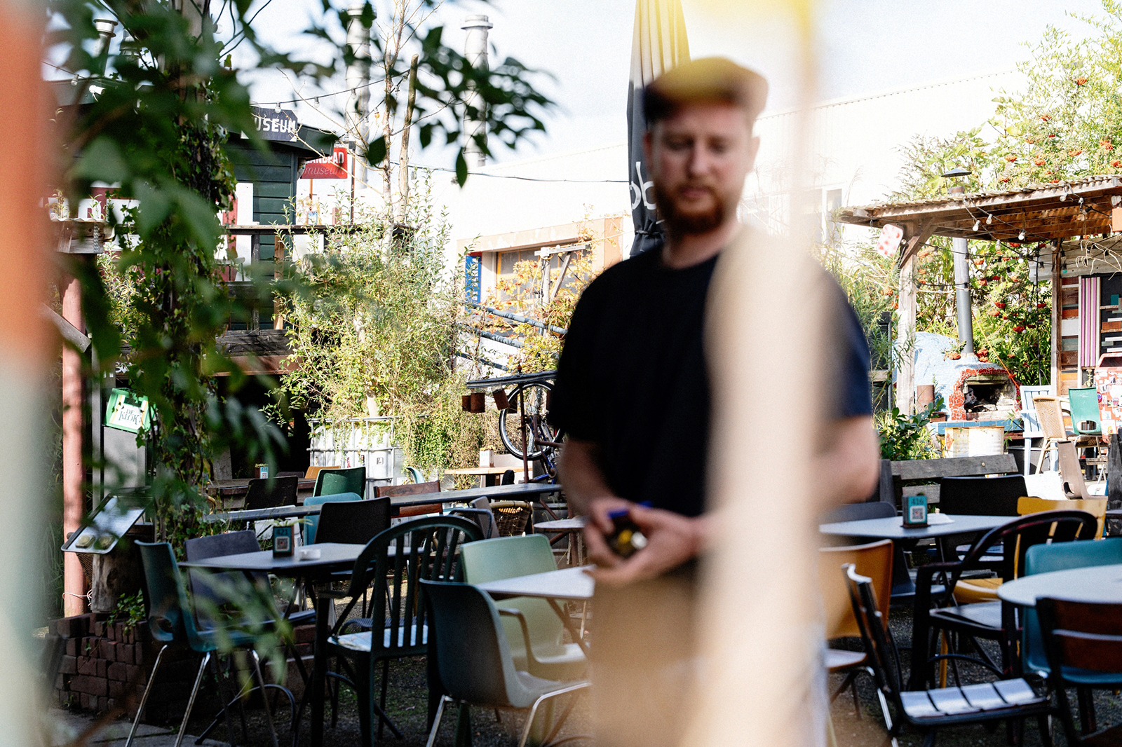 A photo of Jonathan on the terrace of De Nijverheid. Jonathan is out of focus in the photo; the focus is on the terrace, which is filled with tables and chairs.